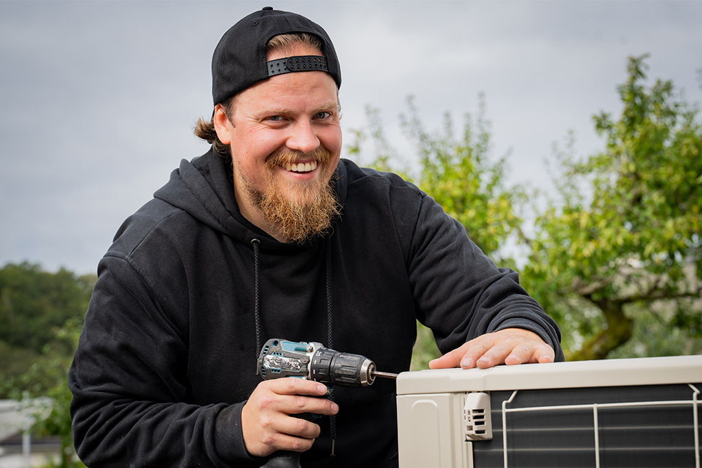 Smilende montør som monterer varmepumpe.